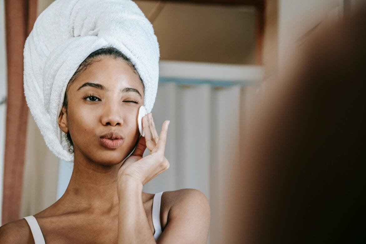 A woman with a towel on her head cleansing face.