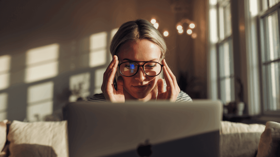 a woman wearing glasses, concentrating while working on a laptop in a well-lit room.