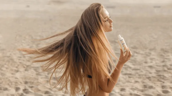 girl with very long blonde hair holding a sunscreen at the beach