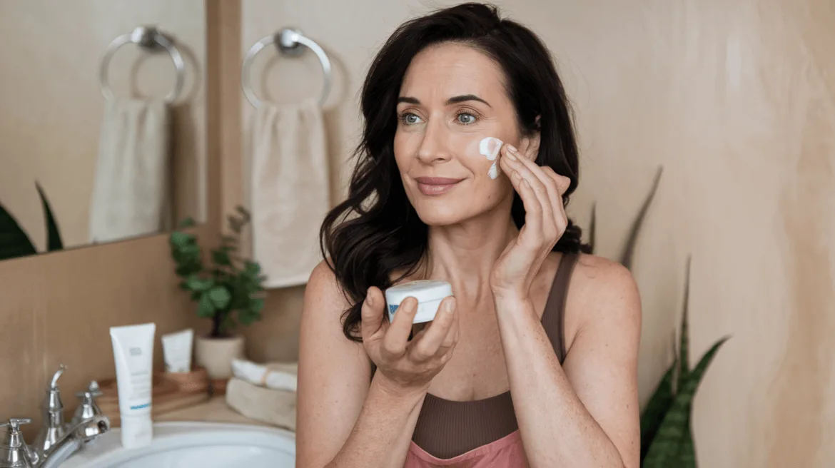 middle age beautiful woman with dark hair is applying face cream on her face