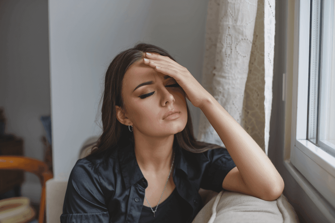 woman with closed eyes and a hand over her forehead, indicating she has a migraine.